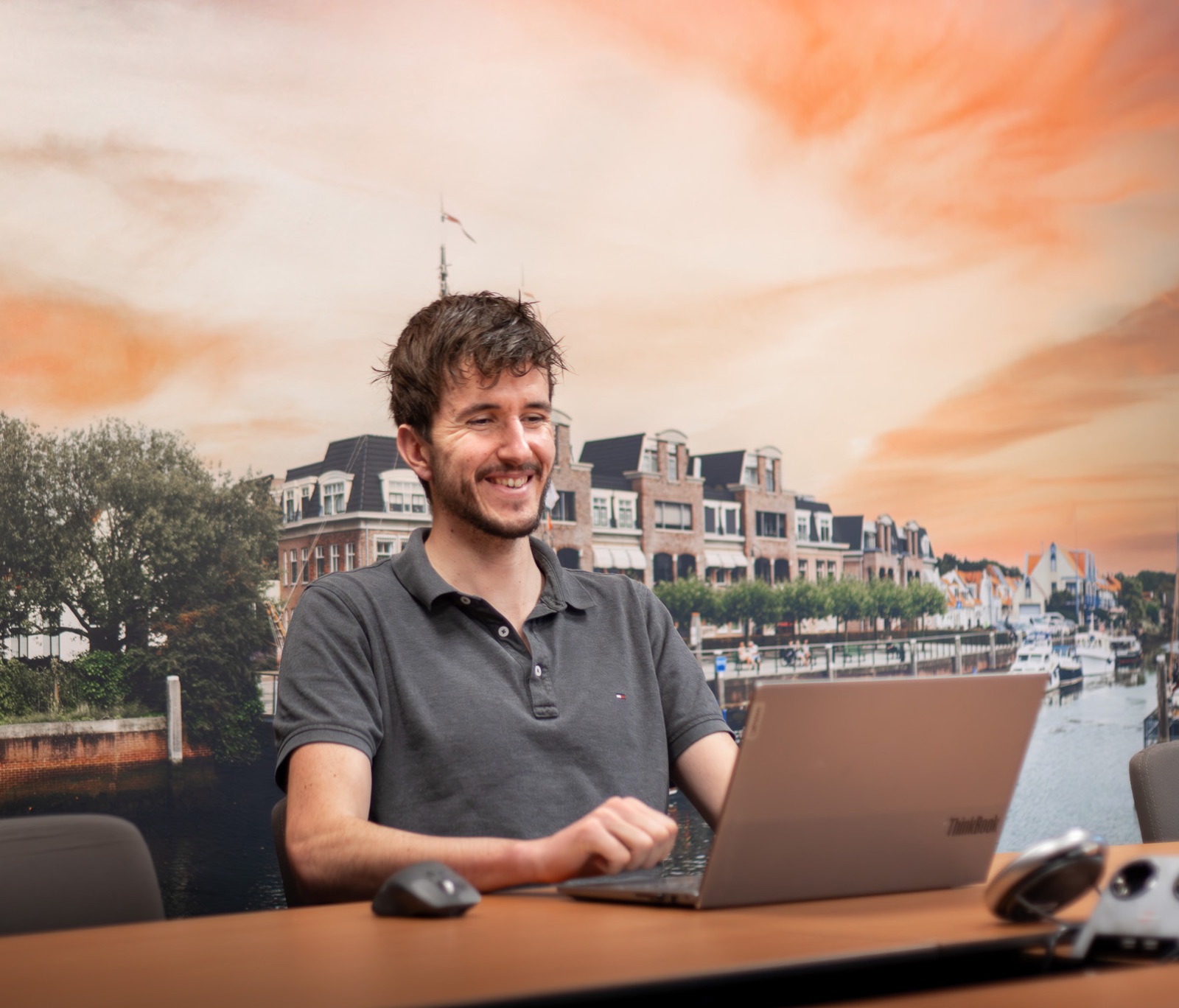 Collega van Invision ICT lacht achter zijn laptop op kantoor, met een fotowand van de haven op de achtergrond